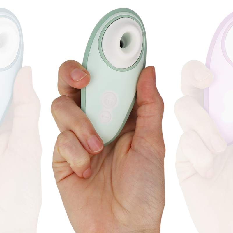 Hand holding light green Womanizer Liberty 2 clitoris stimulator with round suction head and two control buttons.