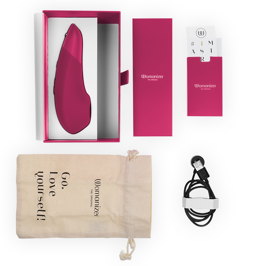 Vibrant pink Womanizer Enhance clitoral stimulator with packaging, drawstring pouch, and USB charging cable.